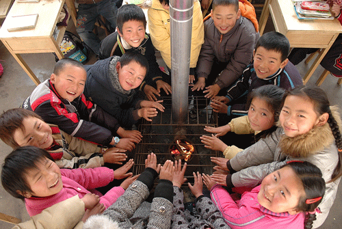 2009年1月6日，山东省日照市东港区南湖镇盛家代疃希望小学三年级一班教室，小学生在火炉旁取暖。