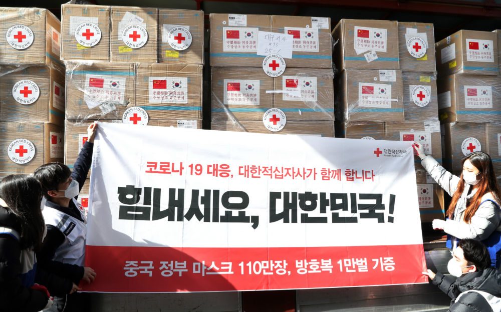3月20日，在韩国仁川，大韩红十字社工作人员将中方援助物资装车后展示助力条幅，上面印有“加油，韩国”的字样。