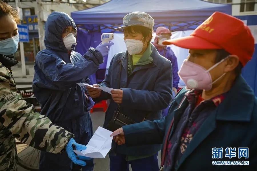 2月22日，在武汉市百步亭社区建设新村，社区工作人员（左一、左二）在出入口查看居民进出凭证，并为居民测量体温。新华社记者　沈伯韩　摄