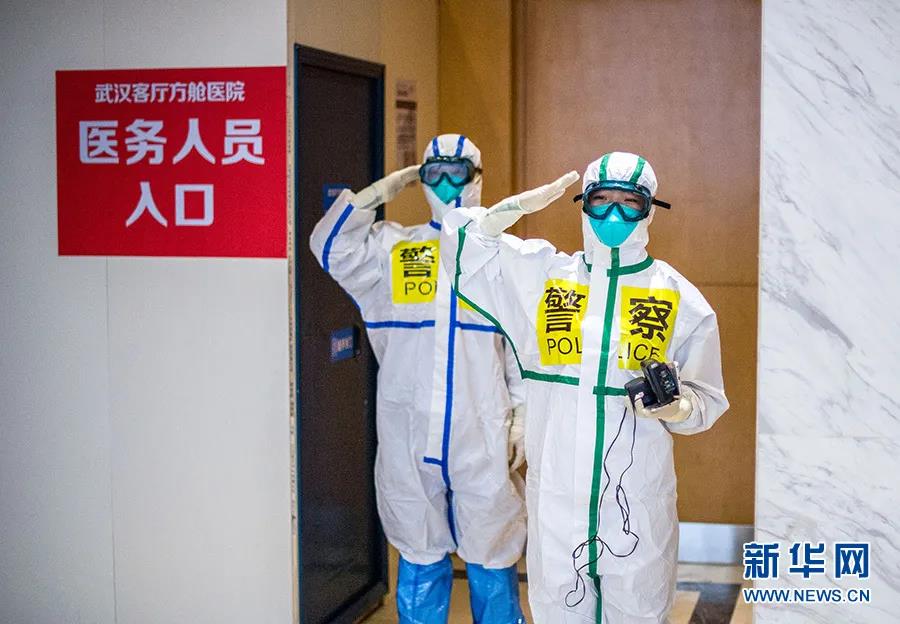 2月25日，在武汉客厅方舱医院，来自武汉市东西湖区公安分局的民警张锦星（右）与同事刘晨在进方舱前向同事敬礼。新华社记者　肖艺九　摄