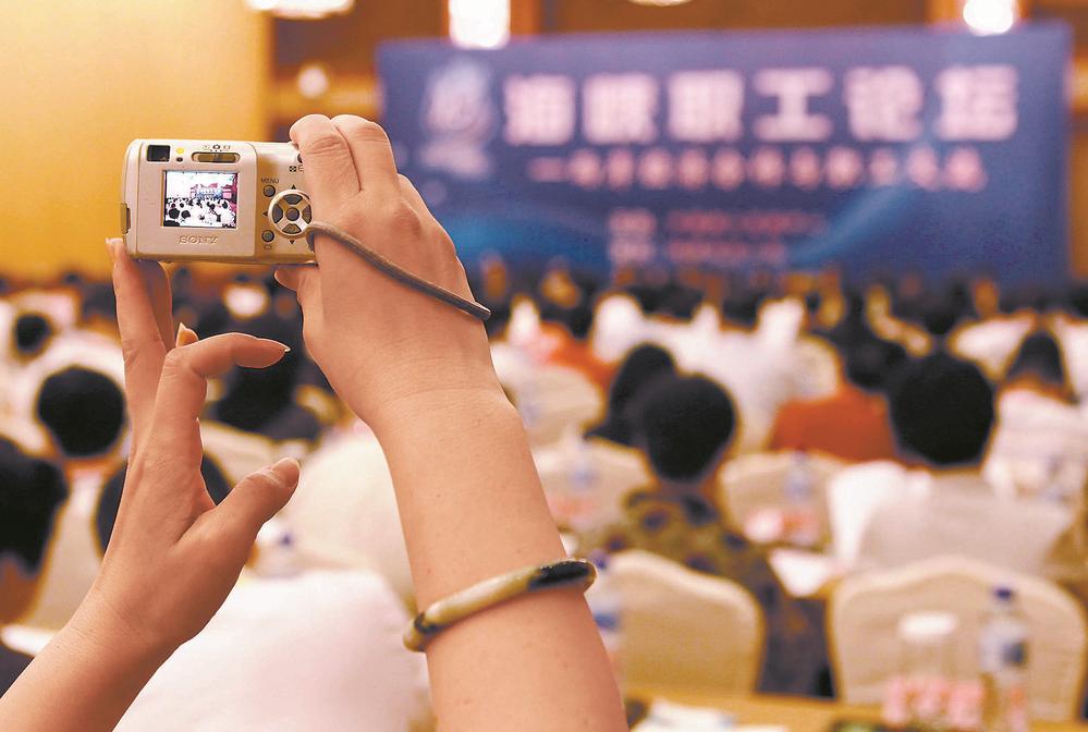 一位与会的台湾代表高举手中的相机记录下海峡职工论坛大会的场景。(资料图片)