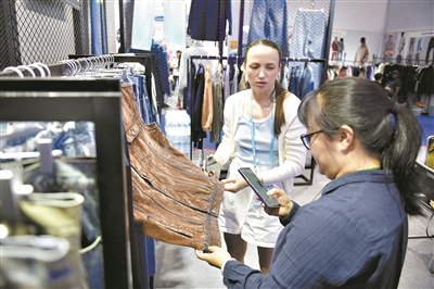 海外客商在广交会内的服装行业展位上咨询商谈。